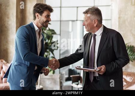 Two businessmen shaking hands in an office setting - Symbol of successful agreement and partnership. Stock Photo