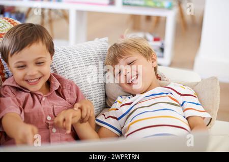 Laptop, kids and happy siblings on sofa for cartoon, film or streaming funny movie at home. Computer, learning or boy children in house for google it Stock Photo