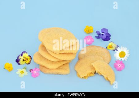 Homemade white chocolate custard cookies with scattered Spring flowers and wildflowers on blue background. Natural comfort food floral nature theme. Stock Photo