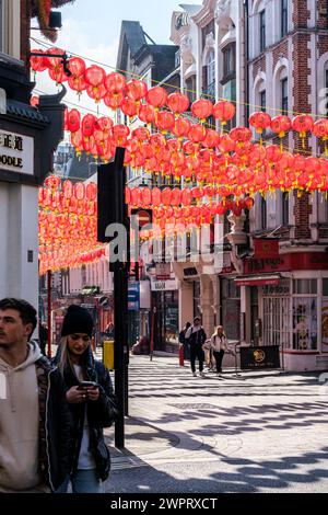 Chinatown, London UK, March 08 2024, Woman Using Mobile Phone Texting Under Orange Lanterns Of Chinatown Street Stock Photo