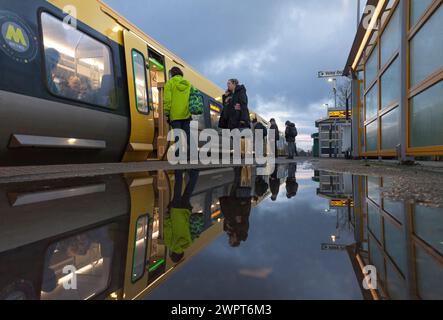 Passengers leaving and boarding a Merserail train at Bebington railway station reflected in a puddle Stock Photo