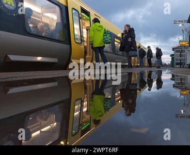 Passengers leaving and boarding a Merserail train at Bebington railway station reflected in a puddle Stock Photo