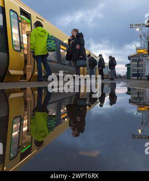 Passengers leaving and boarding a Merserail train at Bebington railway station reflected in a puddle Stock Photo