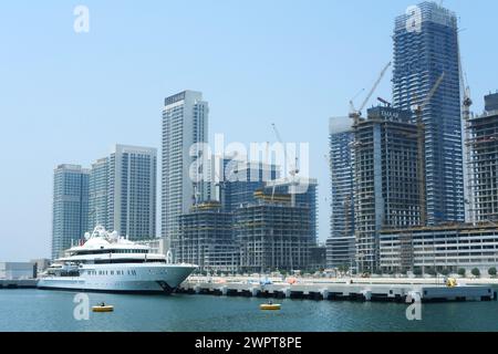 A luxury yacht anchored in front of the bustling construction sites of new high-rise buildings at Dubai Marina. Dubai, UAE - August 15, 2023 Stock Photo