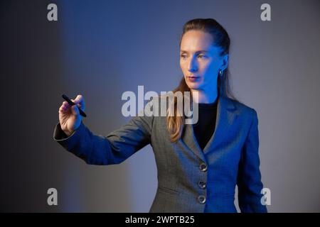 Business woman holding a light pencil in her right hand on a gray background. Focus on the hand. Blue color correction. Stock Photo