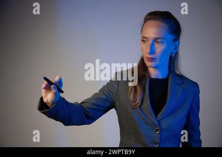 Business woman holding a light pencil in her right hand on a gray background. Focus on the face. Close-up. Blue color correction. Stock Photo