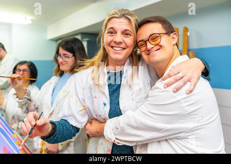 Portrait of a happy man with down syndrome embracing his painting teacher during class Stock Photo