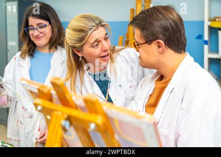 Art teacher talking to a man with down syndrome while painting on canvas Stock Photo