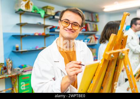 Portrait of a happy man with down syndrome smiling at camera during painting class Stock Photo
