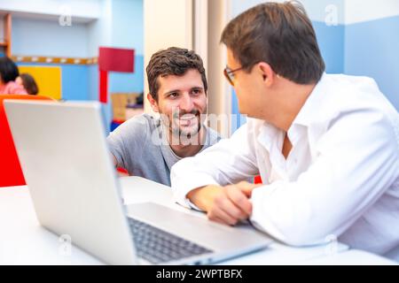 Teacher talking to a man with down syndrome during computing class Stock Photo