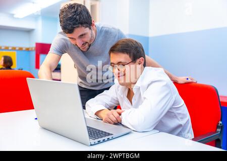 Friendly adult male teacher helping a man with down syndrome during computing class Stock Photo
