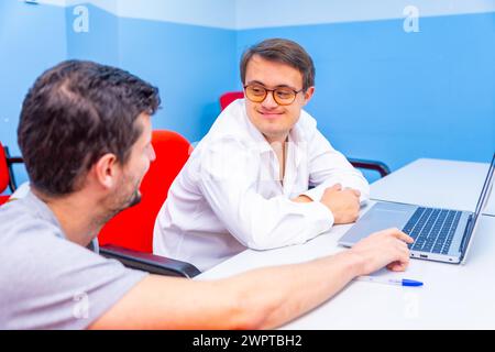Happy and relaxed man with down syndrome and teacher talking during IT computing class Stock Photo