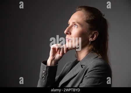 Close-up portrait of a business woman who is thoughtful and looks up. Gray background. Stock Photo