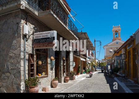 A traditional bakery on a alleyway corner with characteristic stone architecture under a blue sky, alley in old town with church, Koroni Stock Photo