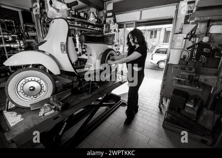 Woman mechanic working on repairing a white moped italian vintage scooter, surrounded by tools in a workshop, real women performing traditional man Stock Photo