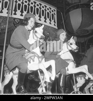 At the amusement park in 1943. Two young women in uniform from the voluntary defense organization Swedish Blue Star at a fairground where they have fun while riding the horses in the carousel. 1943 Kristoffersson ref E114-6 Stock Photo