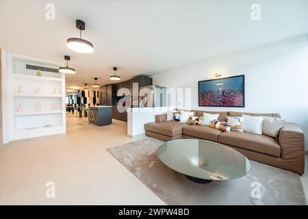 a living room with large brown leather sofa with open kitchen in mediterranean apartment Stock Photo