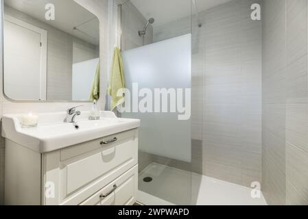 A conventional bathroom with white wooden cabinet, one-piece porcelain sink above the drawer cabinet and frameless mirror Stock Photo