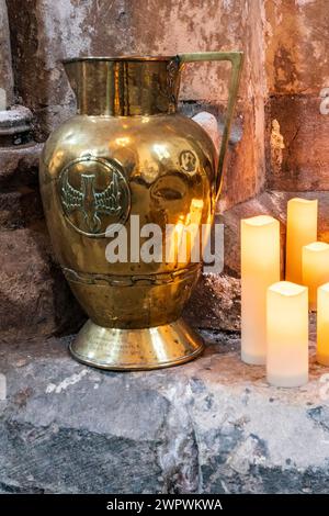 Still life with antique brass jug, lit candles set against ancient stone. Religious theme. Peaceful, antiquity, calming. Stock Photo