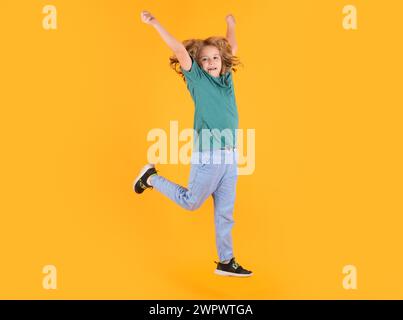 Energetic kid boy jumping and raising hands up on isolated studio background. Full length body size photo of jumping high child boy, hurrying up runni Stock Photo
