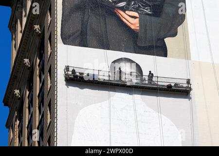 Commercial artists, painters on a suspended scaffold hand painting a billboard advertisement on the side of a high rise building in New York City. Stock Photo