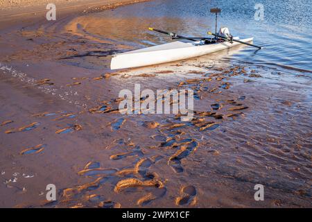 Coastal rowing shell on a muddy shore of Carter Lake in northern Colorado with footprints Stock Photo