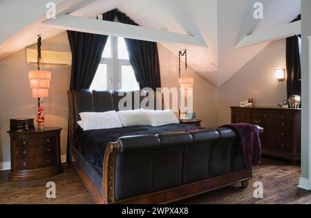 Black leather and brown wood frame king size sleigh bed in master bedroom with hardwood floor inside luxurious home. Stock Photo