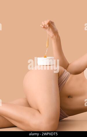 Beautiful young woman holding container with sugaring paste and spatula on brown background Stock Photo