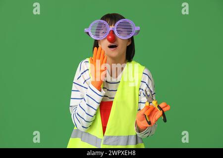 Young surprising female builder with pliers on green background. Fool's day Stock Photo