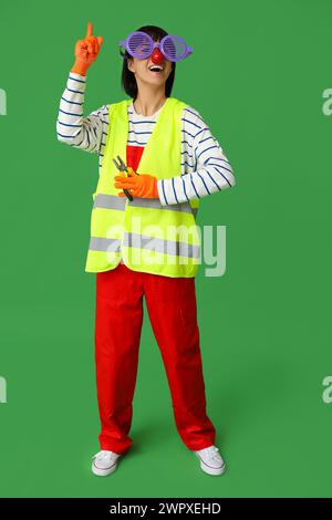 Young laughing female builder with pliers on green background. Fool's day Stock Photo
