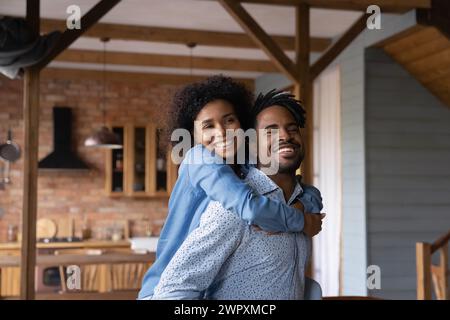 Happy African wife piggyback cuddling husband smiling looking at camera Stock Photo