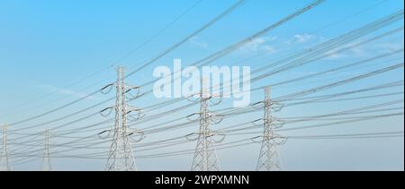 Looking up steel power pylons construction with high voltage cables against blue sky Stock Photo