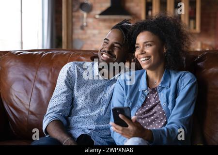 Cheerful African couple sit on sofa at home with cellphone Stock Photo