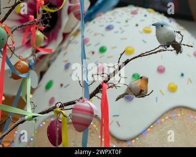 Decorated eggs hanging from a tree branch with a multicolored ribbons and sitting birds, selective focus Stock Photo