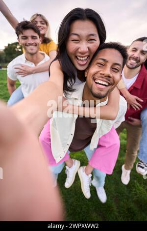 Multirracial group of friends taking selfie picture walking the park hugging by couples and smiling. Stock Photo