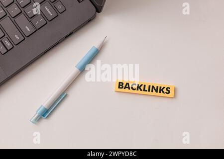 Black laptop, blue pen, yellow sticker has text Backlinks  on the white desk. Concept improve website visibility and rankings on search engines Stock Photo