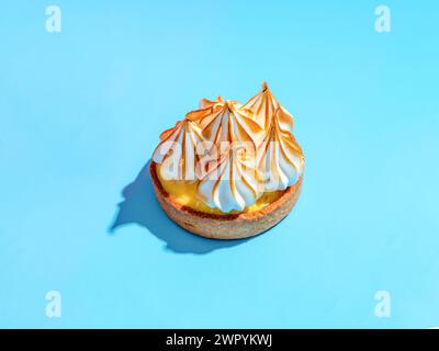 Mini cake decorated with whipped egg whites meringue. Mini lemon tart with burnt French meringue. Delicious dessert with lemon filling. topped with meringue on blue background, hard shadows copy space Stock Photo