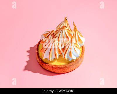 Mini cake decorated with whipped egg whites meringue. Mini lemon tart with burnt French meringue. Delicious dessert with lemon filling. topped with meringue on pink background, hard shadows copy space Stock Photo