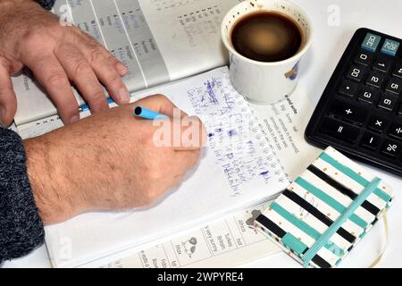 A man sits at a table and writes something in a notebook with a fountain pen, a cup of coffee stands next to him. Stock Photo