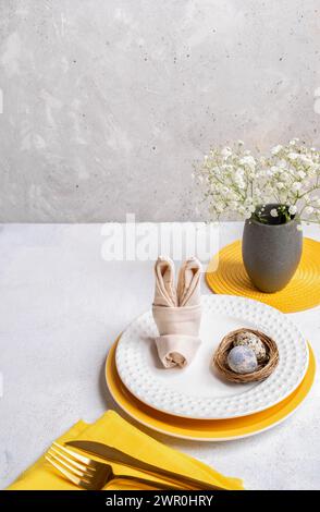 Easter holiday image of table serving idea. Table decoration in white and yellow colors of tableware. Gray and white neutral background. Vertical form Stock Photo