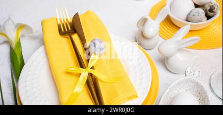 Easter table decorations. Golden cutlery on plates, ceramic bunnies, natural colors eggs, white Iris flower. Fragment of Easter table serving in white Stock Photo