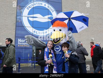 Brighton and Hove, UK. 10th Mar, 2024. Brighton and Hove Albion fans pose with the club mascot while holding an umbrella before the Premier League match at the AMEX Stadium, Brighton and Hove. Picture credit should read: Paul Terry/Sportimage Credit: Sportimage Ltd/Alamy Live News Stock Photo