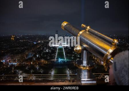 A tourist looks through a telescope from the Eiffel Tower during a rainy day. Stock Photo