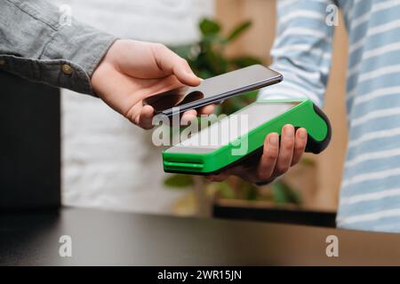 Customer is paying with smartphone in shop using NFC technology. Man doing shopping, buying goods using phone for contactless payment. Contactless and NFC technology Stock Photo