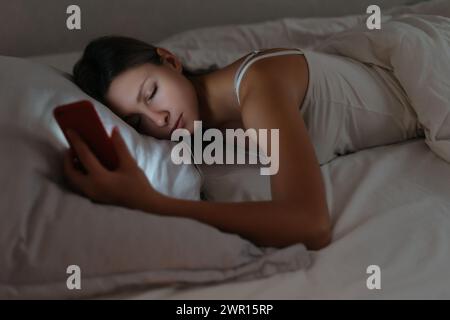 Young woman fell asleep while using smartphone at night. Phone dependence and overuse. Smartphone addiction concept Stock Photo