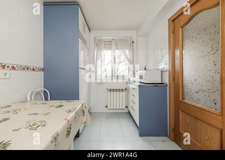 kitchen with blue and white furniture, light blue stoneware floors and wooden and glass access doors to other rooms Stock Photo