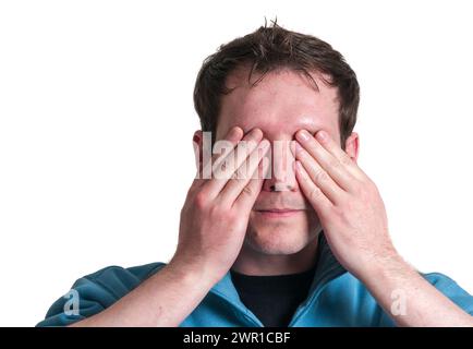 Frontal head portrait of a young brunette Caucasian man holding both hands over his eyes isolated on white. Stock Photo