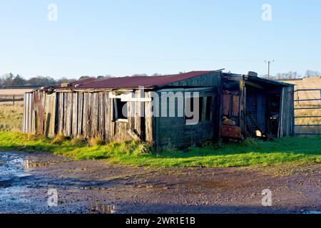 A shot of a ramshackle, dilapidated, derelict wooden farm outbuilding or shed, showing multiple repairs with the roof held down by large rocks. Stock Photo