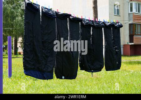 A line of clothes hanging on a clothesline in a backyard, drying in the sun on a clear day. Stock Photo