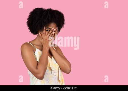 Curly-haired African American woman playfully covers her face with hands Stock Photo
